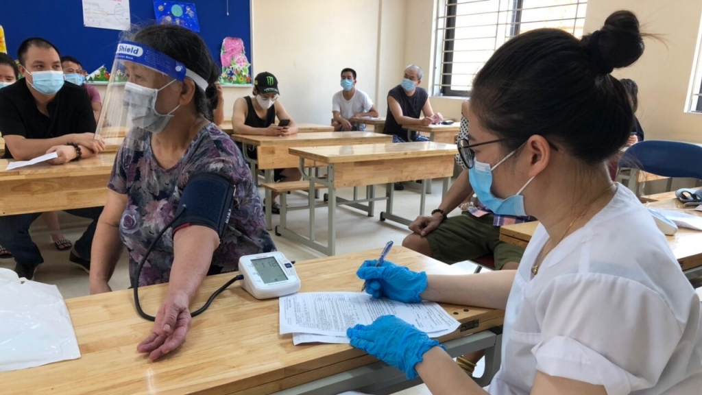 Người cao tuổi được đo huyết áp, khám sàng lọc trước khi tiêm vắc xin